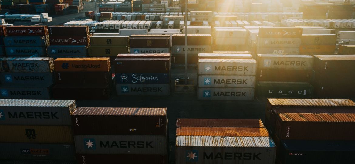 Image shows the storage of many cargo containers in bright sunshine.