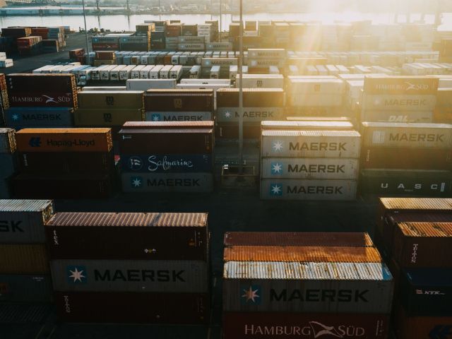 Image shows the storage of many cargo containers in bright sunshine.
